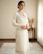Woman in embroidered off-white kurta with blue floral neckline, standing in a bright room