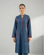 Woman wearing a blue embroidered kurta with pink and purple accents, standing indoors