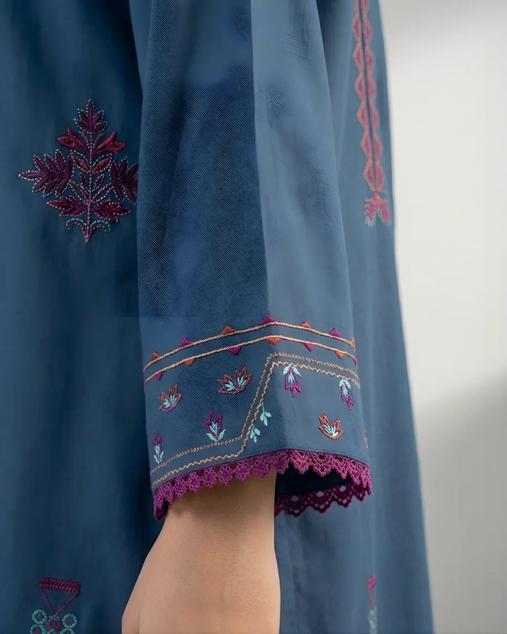 Close-up of blue kurta sleeve with colorful floral embroidery and lace trim