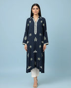 Woman wearing navy embroidered kurta with white trousers and beige heels on blue background